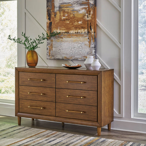 Lyncott brown wood dresser with six drawers and tapered legs in a bright room, with a vase of branches and abstract wall art above it